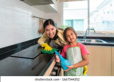 Asian Cheerful Mother And Daughter Cleaning Table Surface With Rag And Spray Bottle Together At Kitchen Counter In House. Happy Family Time To Teaching Daughter To Housework.