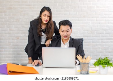 Asian Cheerful Professional Successful Businesswoman Manager Mentor Standing Helping Young Businessman Colleague Sitting Working With Laptop Notebook Computer On Workstation Desk In Company Office.