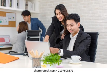 Asian Cheerful Professional Successful Businesswoman Manager Mentor Standing Helping Young Businessman Colleague Sitting Working With Laptop Notebook Computer On Workstation Desk In Company Office.