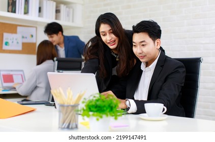 Asian Cheerful Professional Successful Businesswoman Manager Mentor Standing Helping Young Businessman Colleague Sitting Working With Laptop Notebook Computer On Workstation Desk In Company Office.