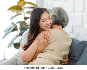 Asian cheerful young beautiful daughter sitting smiling hugging embracing showing affection love comforting bonding with old senior grey hair pensioner mother on cozy sofa in living room at home. - Shutterstock ID 2188779863