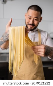 Asian Chef In Apron Holding Raw Spaghetti In Kitchen