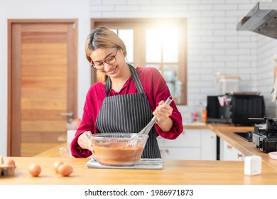 Asian chef woman blend dough and chocolate with beater for cooking chocolate cake with happy feeling in the morning