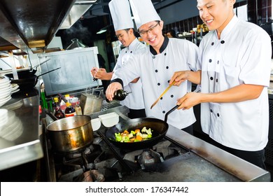 Asian Chefs In Hotel Or Restaurant Kitchen Cooking And Finishing Dishes