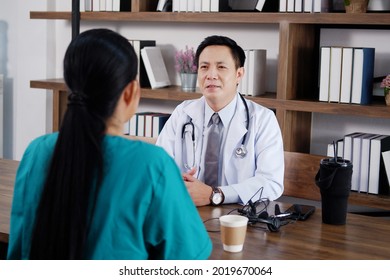 Asian Chief Physician Man Is Brainstorming With Surgeon Doctor Woman Wears Green Surgical Gown. Medical Team Are Talking And Researching With Laptop For Treatment In Meeting Room At Hospital.