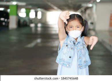 Asian Child Angry Thumb Down Or Kid Girl Dislike Wearing N95 White Face Mask For Close Mouth Nose With Flu Sick And Protect PM2.5 Dust By Car Park Smoke Or Covid-19 Coronavirus And Not Good Symbol