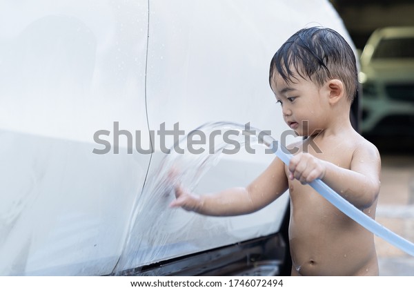 Asian child baby boy washing\
car, wash with luxury white car at home, in the garden on summer\
day.