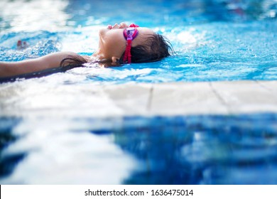 Asian Child Backstroking In The Deep Pool.Active Kid Swimming During Competition. Sports Activity. Girl Wearing Goggles In Blue Water.Fun Leisure Activity .