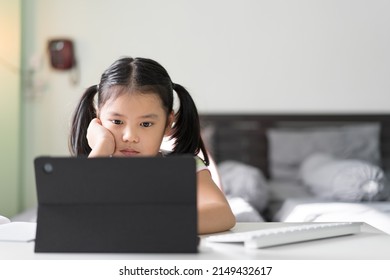 Asian Child Bored Learning By Study Online Class On Computer Tablet Or Kid Girl Student Back To School By Video Call Studying And Hand To Cheek Or Person Learn From Home By Reading On Pad In Bedroom