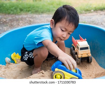 Asian Child Boy Playing Car Toy In Sandbox Outdoor In Rural Nature Background With Smiling Face. Happy Kid Enjoy In Relaxing Day.