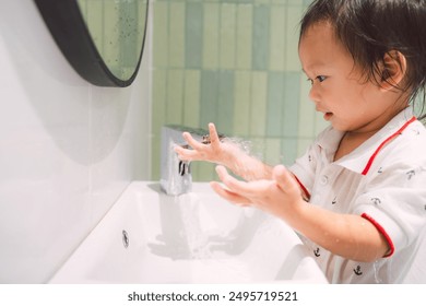 Asian child boy is practicing good hygiene by washing their hands in a bathroom with fun. Independent toddler washing hands alone at sink. Kid aged 1-2 years old. - Powered by Shutterstock