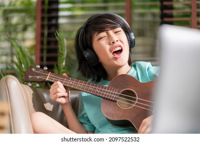 Asian Child Boy Sing Lound While Learn Online Ukulele Study Course With Fun And Exiting At Home,online Study Stay Home Concept Asian Child Playing Ukelele And Sing In Living Room At Home