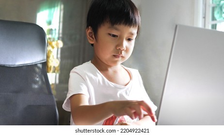 Asian Child Boy Using Laptop For Studying At Home. Kid Type Keyboard On Notebook With Serious Face. Online Education Learning, Home School Concept.