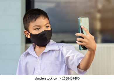 Asian Child Boy Wearing Black Fabric Mask On His Face For Prevent Covid-19 Disease And Corona Virus. He Using A Smart Phone For Study Online At Home. Stay Safe And Social Distancing. 6-7 Years Old Kid