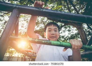 Asian Child Climbing And Having Fun At Adventure Park. Handsome Boy Smiling Happily At Children Playground. Outdoor With Bright Sunlight On Summer Day. Vintage Film Filter Effect.