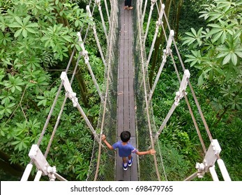 Asian child crossing a simple suspension rope bridge above tropical forest - Powered by Shutterstock