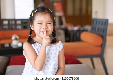 Asian Child Cute Or Kid Girl Smile With Laugh Squat And Forefinger Close Mouth For Tell Quietly Shh Or Stop Silence And Secret Surprise With Play Hide And Seek At Library At School Or Reception Room