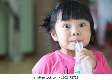 Asian Child Cute Or Kid Girl Enjoy Drinking Water Or Soy Milk Beverage And Milkshake In Bottle By Tube Or Straw For Dessert And Protein With Make Face Refreshing And Big Eye And Wear Pink Shirt