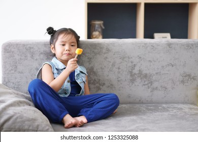 Asian Child Cute Or Kid Girl Happy And Enjoy Delicious Eating Orange Ice Cream For Sweet Dessert And For Refresh On Summer And Sofa At Kindergarten Or Home Preschool And Nursery With Wear Jean