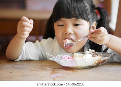 Asian Child Cute Or Kid Girl Enjoy Eating Banana Split Ice Cream With Chocolate For Sweet And Cold Dessert By Left Handed On Wooden Table And Window Side In Restaurant On Preschool Summer