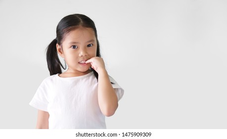 Asian Child Cute Or Kid Girl Nail Biting On Finger And Smiling With Anxious Or Thinking Enjoy On Preschool Or 5 Years Old And Wear White T-shirt And White Background Isolated With Copy Space