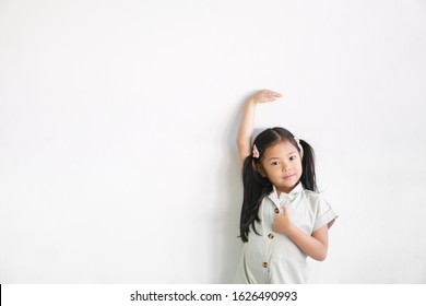 Asian Child Cute Or Kid Girl Happy Smile Show Height And Measure Tall With Growth By High Hand And Arm Up With Show Thumb Finger For Like And Good On Empty White Wall Background Isolated With Space