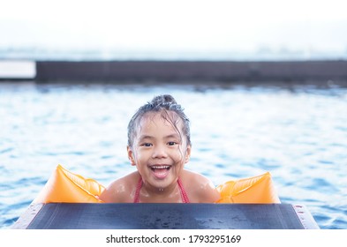Asian child cute or kid girl smiling swim and wear swimming armband or life jacket with vacation happy fun on pool chair or bed and waterpark for fresh with health exercise and summer holiday travel