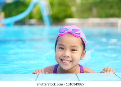 Asian child cute or kid girl wear swimming suit and goggles on swimming pool and smile with happy fun in water park for learn and training swim or refreshing and relax with exercise on summer holiday