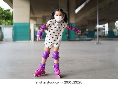 Asian Child Cute Or Kid Girl Exercise Playing Pink Rollerblade Or Inline Skates On Sport Skating Rinks Or Park And Wearing Knee To Wrist Support And Elbow Pads With White Face Mask For Safety Protect