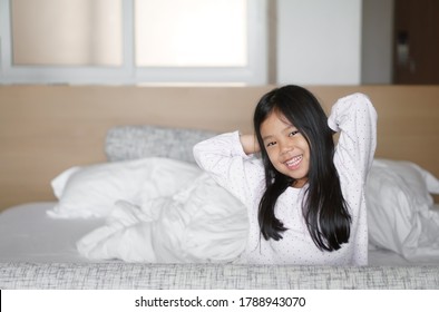 Asian child cute relax or kid girl happy smiling wake or woke up with stretch oneself for refreshing in morning on white bed and pillow in bedroom at home or hotel on holiday travel and vacation
