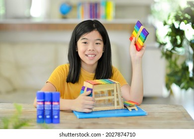 Asian Child Doing Popsicle Stick Craft.School Kid With Colorful Homemade Wooden Sticks House.Creative Idea For Fun Activity In Class.Colorful Sticks.Glue On Table.Homeschooling Projects.