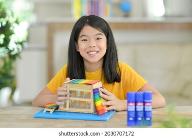 Asian Child Doing Popsicle Stick Craft.School Kid With Colorful Homemade Wooden Sticks House.Creative Idea For Fun Activity In Class.Colorful Sticks.Glue On Table.Homeschooling Projects.