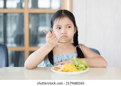 Asian Child Frowning Or Kid Girl Unhappy And Don't Like Eating Vegetables Salad With Corn Tomato And Greens Vegetable With Holding Spoon Or Person Anorexic Bored Food At Kitchen School Or Restaurant