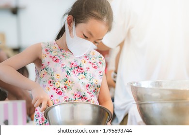 Asian Child Girl In Cooking Workshop For Kid, Holding Kitchen Equipment, Wearing Protective Medical Mask, Child Girl Wearing Floral Pattern Dress, Space For Text.