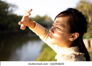 Asian child girl covering face by hand to protect,prevent face skin from bright sun in outdoor summer,female people hand covered the strong sun light feeling hot uncomfortable,risk of eyes damage 