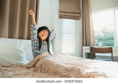 Asian child girl enjoys sunny morning. Good time at home. Kid wakes up from sleep. child girl wakes up in morning in bed and stretches by window. morning awakening little child girl in bed. - Powered by Shutterstock