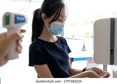 Asian child girl in a face mask use automatic alcohol gel dispenser,spraying on hands and check body temperature with infrared digital forehead thermometer at screening point for COVID-19,Coronavirus - Powered by Shutterstock