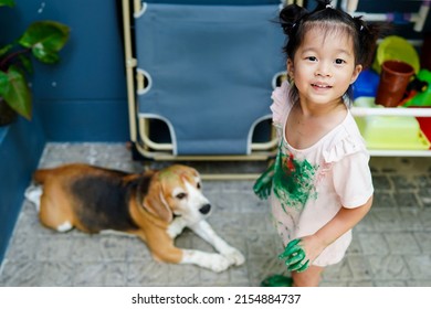 Asian Child Girl With Her Dirty Shirt Pretend To Hold Dog Head While It Laying Down On Tile Floor.Child Try Put Dirty Hand On Beagle Head,it Give Away To Her,close Friend Funny Drawing Activity.