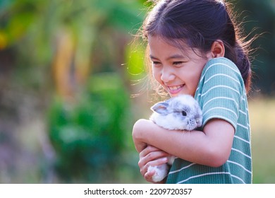 Asian child girl holding and hugging her adorable bunny fluffy with tenderness and love. Kid take care and play with pet in the garden. Symbol of Easter day. - Powered by Shutterstock