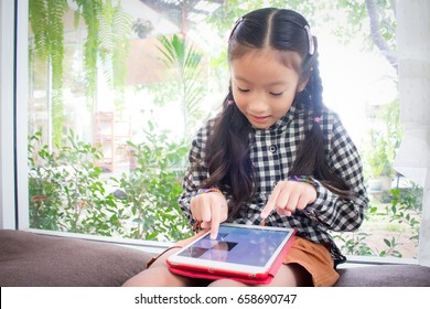 Asian Child Girl Look Smart Phone.kid Is Playing On Ipad 