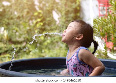 Asian Child Girl Spit Water From The Mouth While Playing Water In The Basin. Happy Girl In The Garden.