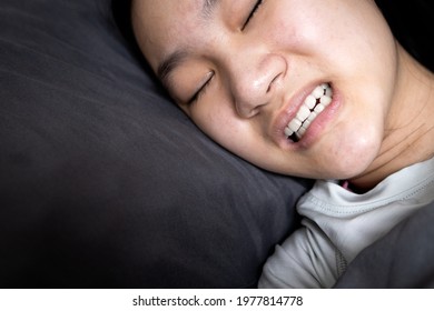 Asian child girl suffering from bruxism while lying in bed at night,female grinding of the teeth during sleep,teeth clenching,sleep disorders,oral health problems,dental care medical,bruxism concept