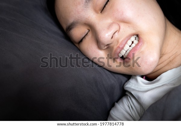 Asian child girl suffering from\
bruxism while lying in bed at night,female grinding of the teeth\
during sleep,teeth clenching,sleep disorders,oral health\
problems,dental care medical,bruxism\
concept