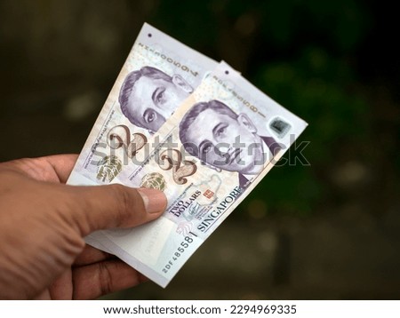 An Asian child holds 2 Singapore dollar banknotes, shallow focus