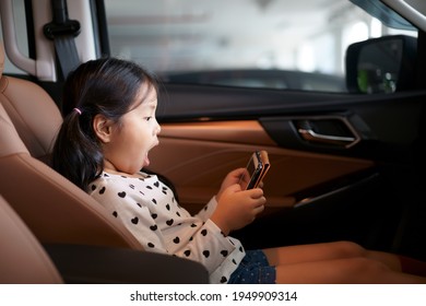 Asian Child Or Kid Girl Enjoy Excited Learn Or Play And Watching Computer Tablet Or Study Online To E-learning By Smartphone And Open Mouth Wow On Car Seat In Car On Street Or People Play Game In Pad