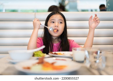 Asian Child Or Kid Girl Enjoy Eating Carrots By Fork And Vegetables Salad With Variety Foods Or Cuisine And Milk Drink At School Kitchen Or Restaurant And Food Court For Breakfast Or Lunch And Dining