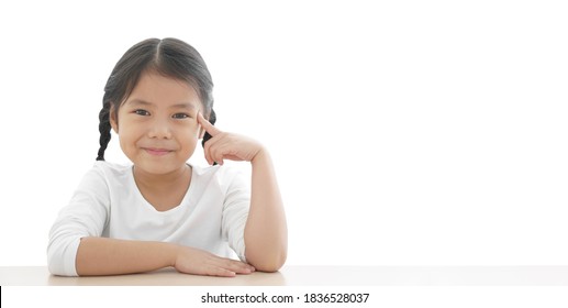 Asian Child Or Kid Girl Finger Point Eye Or Brain Head For New Idea Think And Imagination Or Creativity Education With Smiling Happy At Nursery Pre School On Table And White Space Background Isolated