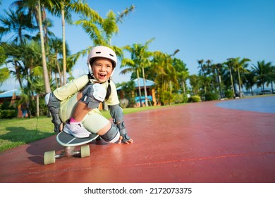 Asian Child Or Kid Girl Fun Playing Skateboard Or Surfskate With Crouching Turn Or Sit Snap In Skate Park And Extreme Sports To Wearing Helmet Elbow Pads Wrist And Knee Support For Body Safety Protect