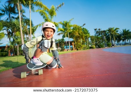 asian child or kid girl fun playing skateboard or surfskate with crouching turn or sit snap in skate park and extreme sports to wearing helmet elbow pads wrist and knee support for body safety protect