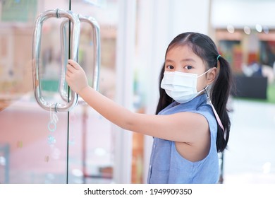 Asian Child Or Kid Girl Holding Glass Door Handle At School Or Mall And Wearing N95 White Face Mask For Close Mouth Nose And Flu Cough Sick And Protect PM2.5 Dust Or Influenza Covid-19 Coronavirus